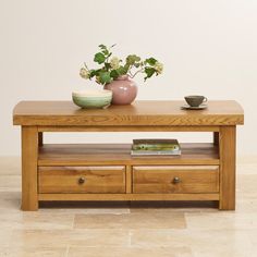 a coffee table with two drawers and a vase on top, in front of a white wall