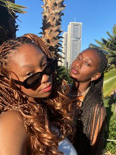 two beautiful young women standing next to each other in front of palm trees and buildings