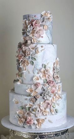 a three tiered wedding cake with flowers on the top and bottom, sitting on a silver platter