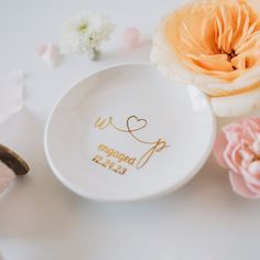 a white plate with gold lettering on it next to flowers