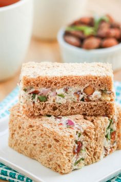 two sandwiches cut in half sitting on top of a white plate next to a bowl of nuts