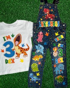 two children's clothing laying on the grass next to each other, one with an image of a dinosaur