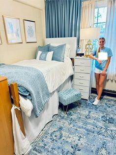 a woman standing next to a bed in a room with blue carpet and white walls