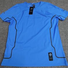 a blue t - shirt with black buttons on it sitting on the floor next to a pair of headphones