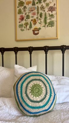 a crocheted round pillow sitting on top of a bed next to a painting