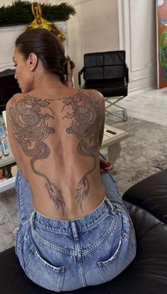 a woman sitting on top of a black leather couch next to a fire place with a dragon tattoo on her back