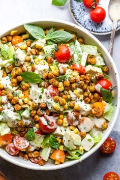 a salad with tomatoes, lettuce and chickpeas in a white bowl