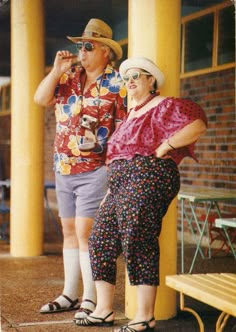 an older man and woman standing next to each other in front of a yellow building