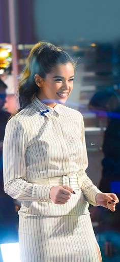 a woman in a white dress smiles as she walks down the runway with her hand on her hip