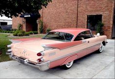 an old pink and white car parked in front of a brick building next to a tree