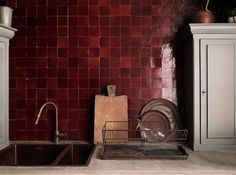 a kitchen with red tiled walls and white cupboards next to a metal dishwasher