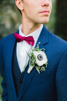 a man in a blue suit with a red bow tie and anemone boutonniere