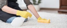 a woman cleaning the carpet with yellow gloves on her feet and holding a rag in one hand