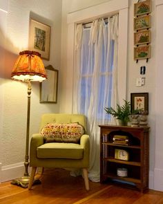 a green chair sitting next to a lamp on top of a wooden table in front of a window