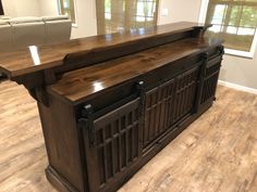 a large wooden bar in the middle of a living room with hardwood floors and windows