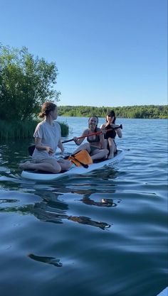 three women are sitting on a paddle boat in the water and one woman is holding an oar