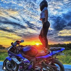 a person standing on top of a motorcycle in the middle of a field at sunset