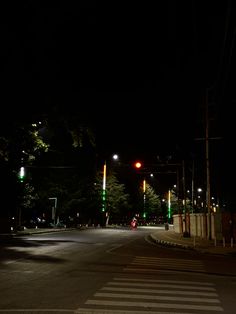 an empty street at night with green and red traffic lights on the side of it