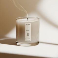 a candle with a white label on it sitting in front of a light brown background