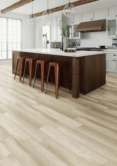 a large kitchen with white cabinets and wooden flooring, along with bar stools