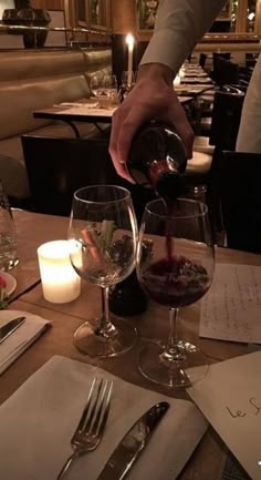 a person pouring wine into two glasses at a table with candles and menus on it