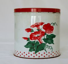 a red and white flowered canister with polka dots on the bottom that has flowers painted on it