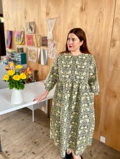 a woman standing in front of a table with flowers on it and holding out her hand