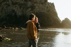 two people are standing on the beach looking out at the water