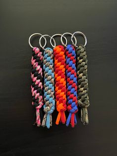 four different colored keychains with metal rings on black background, one is multicolored and the other has an orange, blue, green, red, yellow, pink, purple, and white