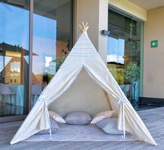 a teepee tent with pillows on the floor in front of a building and glass windows