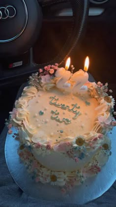 a birthday cake with two lit candles on it sitting in the middle of a car