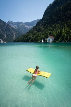 a woman is in the water with a surfboard on her back and mountains in the background