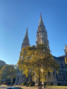 an old church with tall spires and trees in the foreground on a sunny day