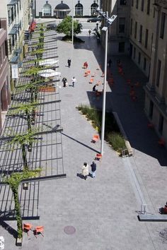 people are sitting on benches in the middle of an open courtyard with tall buildings and trees