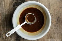 a white bowl filled with brown sauce on top of a wooden table next to a spoon