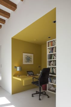 an office with yellow walls and white flooring is seen from the hallway to the living room