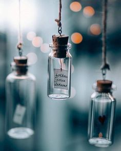 three glass bottles hanging from strings that say love is in the air and are filled with tiny hearts