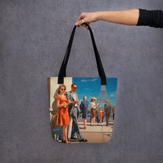 a woman's hand holding a tote bag with an image of people walking in front of the eiffel tower