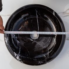 a person measuring the width of a black marbled bowl with a tape around it