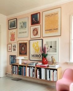 a pink chair sitting next to a bookshelf filled with lots of books and posters