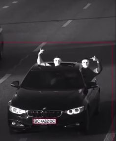 two men waving from the roof of a black car