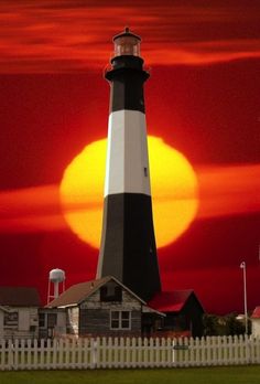 a black and white lighthouse in front of a red sky with the sun behind it