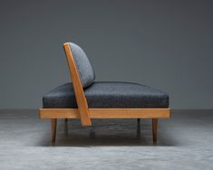 a wooden chair with a black seat and back rest on concrete flooring in front of gray wall