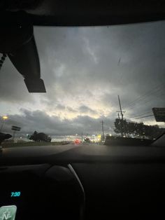 the view from inside a car driving down a road at night with dark clouds in the sky