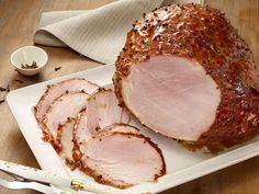 sliced ham on a white platter with knifes and fork next to it, ready to be cooked