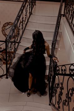 a woman in a black dress walking down some stairs