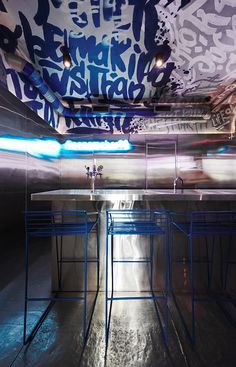 an empty room with blue stools and graffiti on the wall above it is lit by bright lights