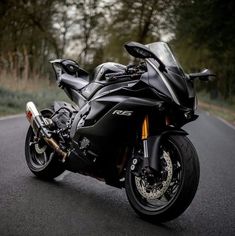 a black motorcycle is parked on the side of the road near some trees and bushes