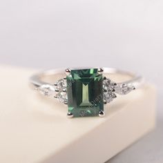 an emerald and diamond ring sitting on top of a white box