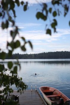 a small boat is docked at the end of a pier on a lake with trees in the background